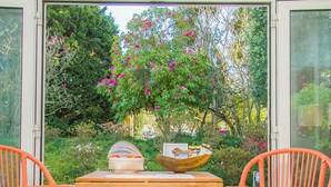 A patio with two orange wicker chairs, a wooden table, and a bowl of fruit. - Liiiving in Porto Garden Pool House (Porto)