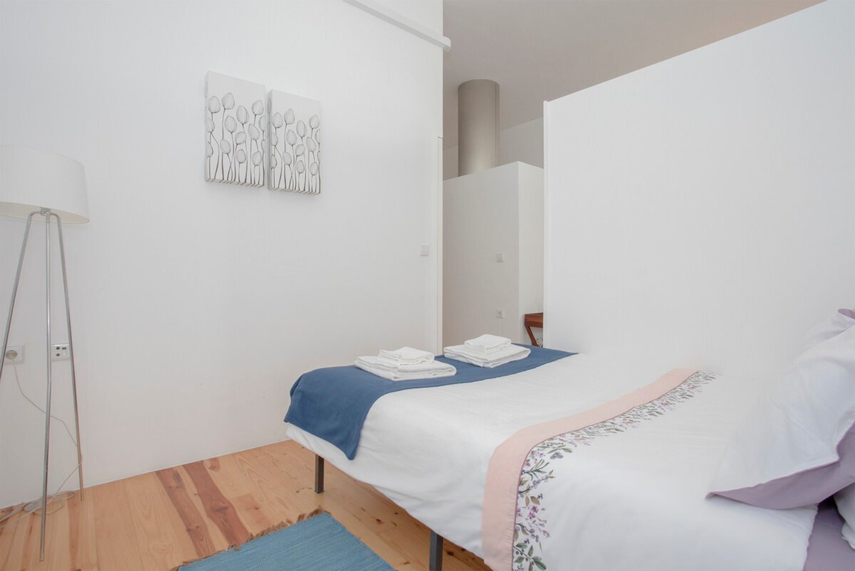 A bedroom with a bed, a blue throw blanket, and a white wall with a geometric art piece.