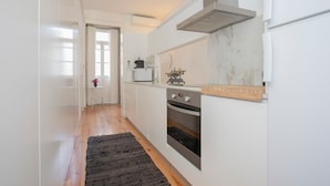 A narrow kitchen with white cabinets, a built-in oven, and a microwave. - Liiiving In Porto Bolh o Market Apartment I (Porto)