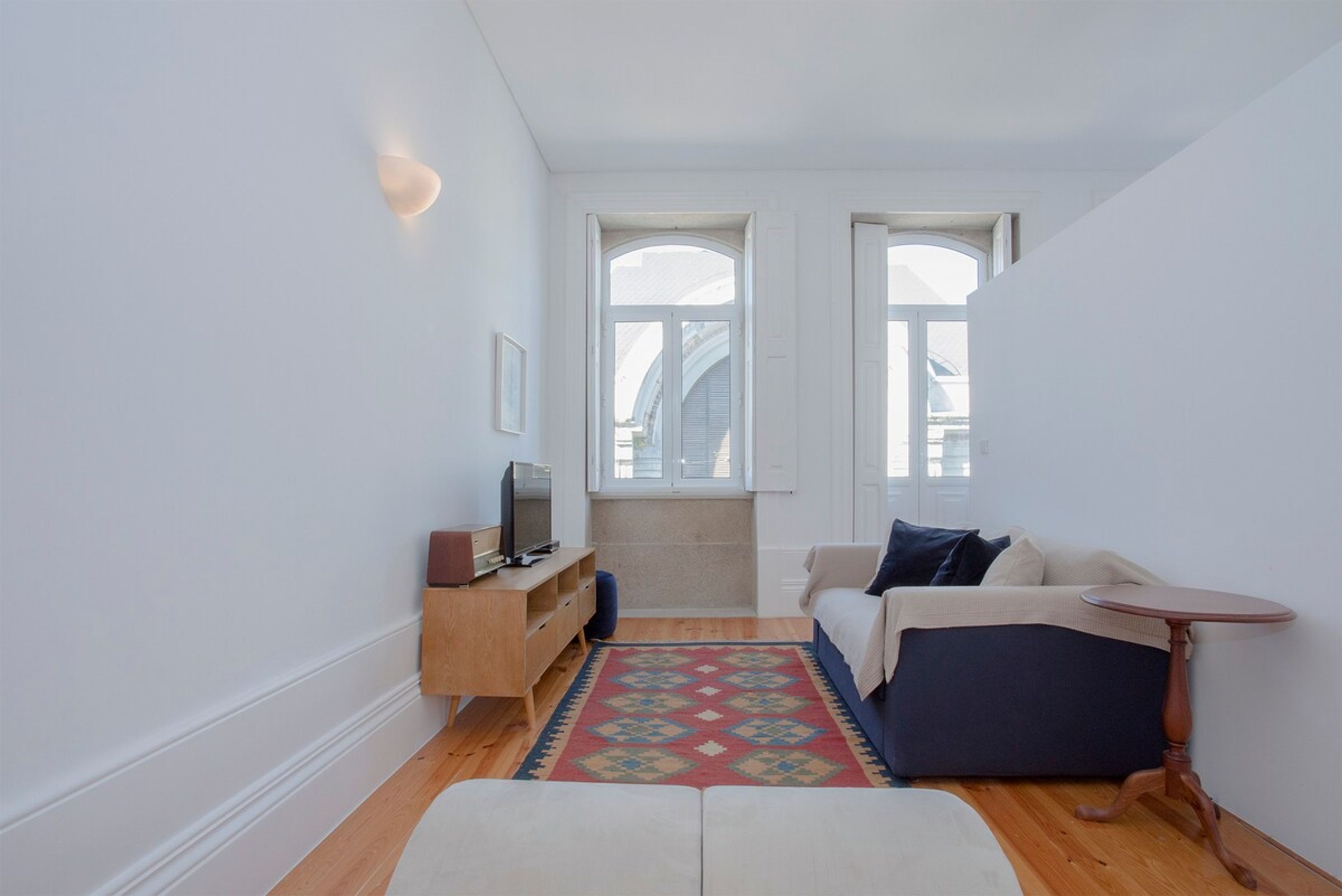 Un espacio habitable compacto con un sofá, una mesita, un televisor sobre un mueble de madera y un tapete estampado.