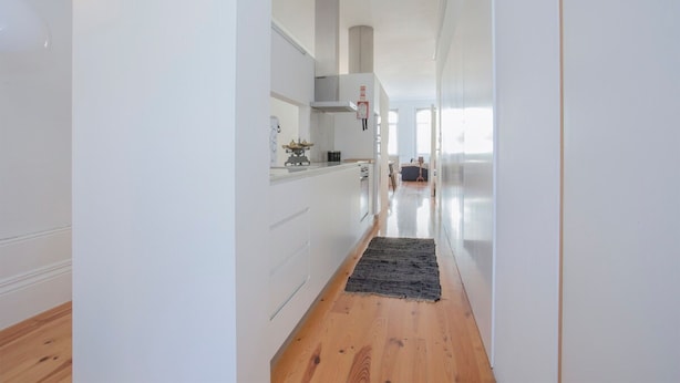 A modern kitchen with white cabinetry, a wooden floor, and a black rug leading to a dining area. - Liiiving In Porto Bolh o Market Apartment I (Porto)