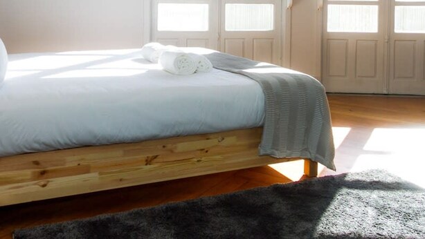 Une chambre avec un lit en bois, une literie blanche et un plaid gris.
