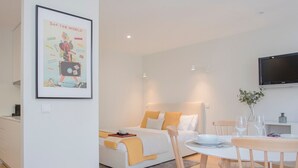 Une chambre moderne et bien éclairée, équipée d’un lit, d’une table à manger avec des chaises et d’un téléviseur fixé au mur.