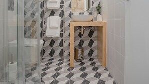 Une salle de bain moderne avec un carrelage aux motifs géométriques, une douche en verre, un meuble-lavabo en bois et un grand miroir.