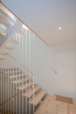 A modern staircase with wooden steps and white railings, leading to a white door with a small window. - Liiiving in Porto Charming Downtown Delight II (Porto)