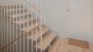 Een moderne trap met houten treden en witte leuningen, die leidt naar een witte deur met een klein raam.