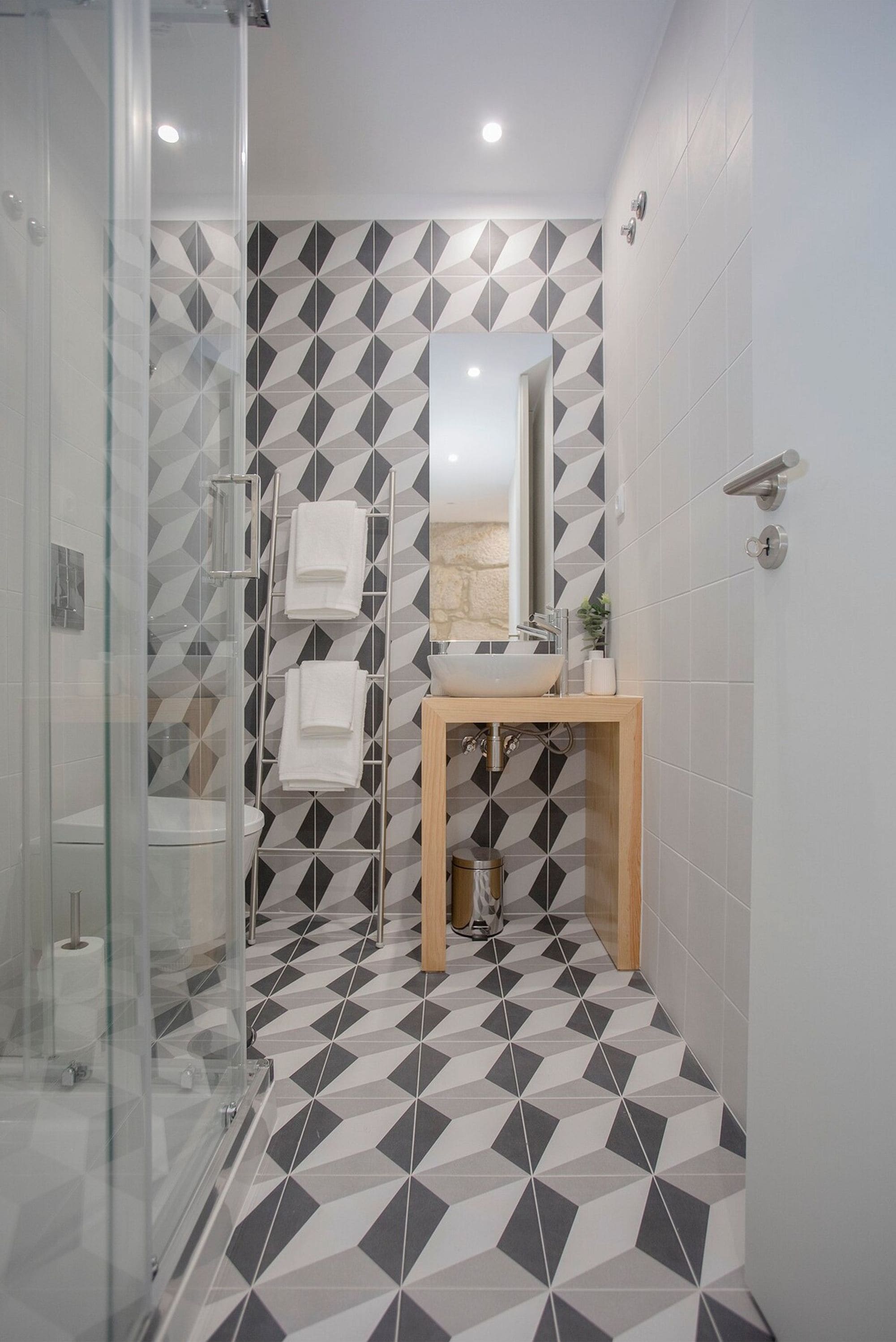 A modern bathroom with a geometric tile floor, a glass shower enclosure, a wooden vanity, and a mirror above the sink.