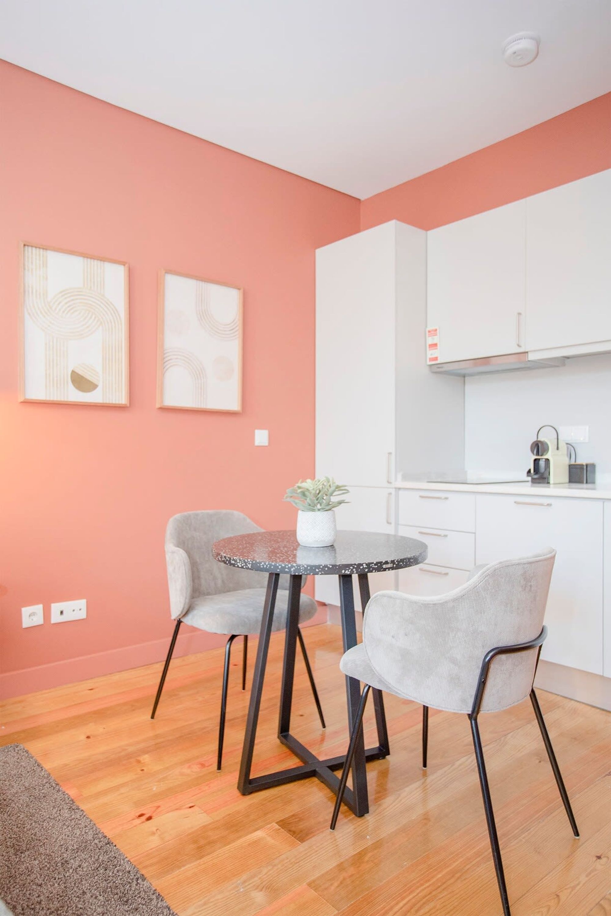 Une cuisine moderne avec des meubles blancs, une table ronde accompagnée de deux chaises et une plante en pot posée sur la table.