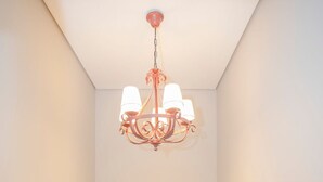 Ein schmaler Flur mit einer Kandelaber, einem grünen Fluchtschild und einer Holztreppe, die zu einem Raum führt.