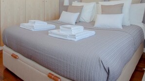 Un lit bien fait, avec des oreillers blancs et beiges, une couverture rayée grise et des serviettes blanches pliées posées sur le lit.