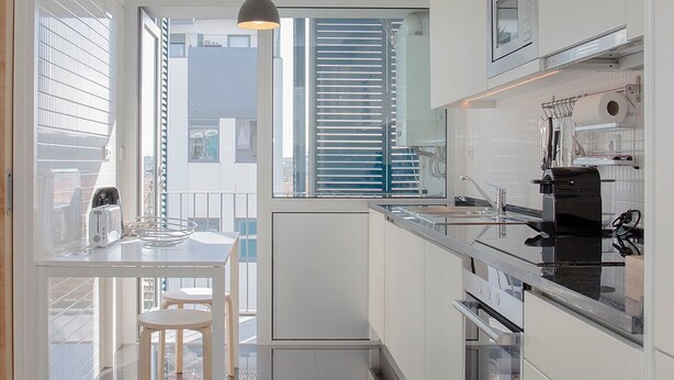 Une cuisine moderne avec des meubles blancs, un plan de travail noir et un luminaire suspendu.