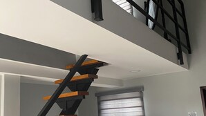 Un intérieur moderne avec un escalier, une fenêtre avec des stores et un coussin jaune sur un canapé noir.