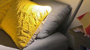 Un lit avec un oreiller jaune et un oreiller gris, une table de chevet avec une lampe et une prise électrique au mur.