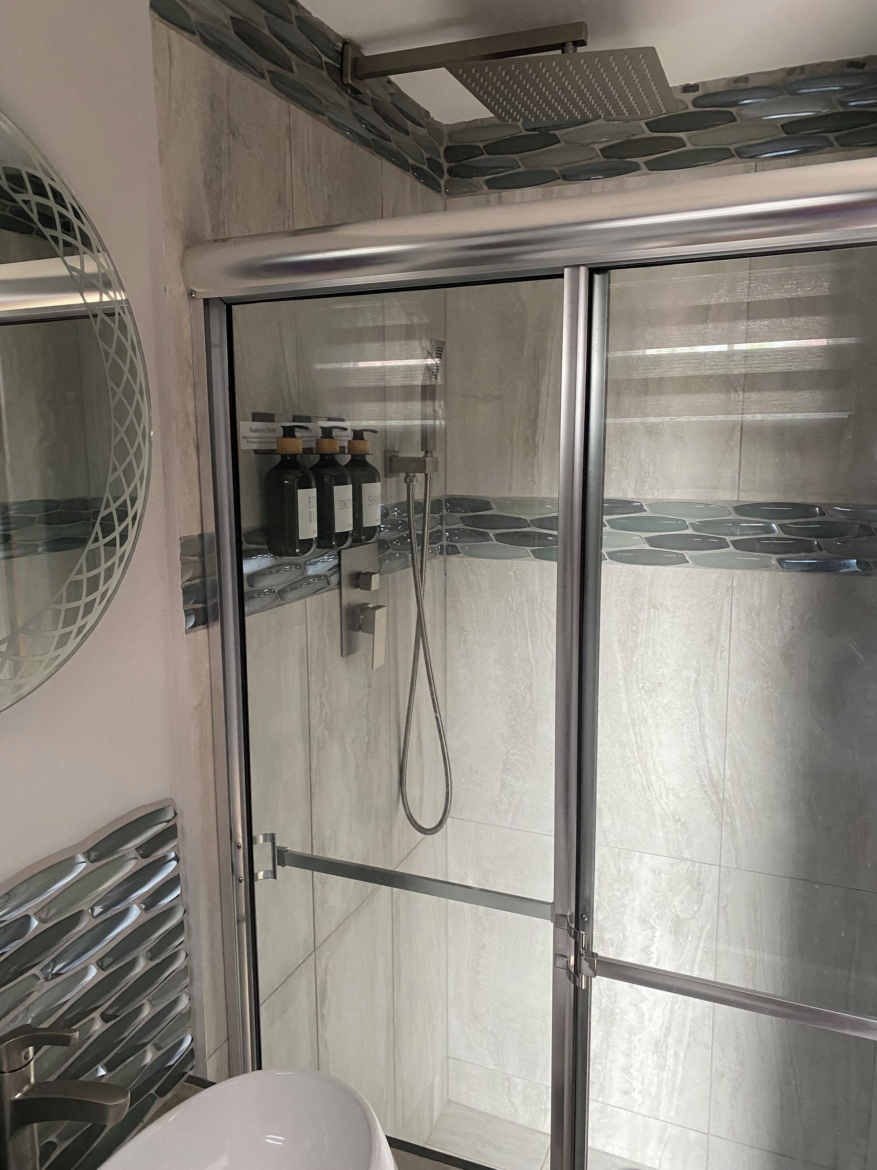 Une salle de bain moderne avec une douche à parois de verre, un lavabo blanc et un miroir doté d’un cadre décoratif.