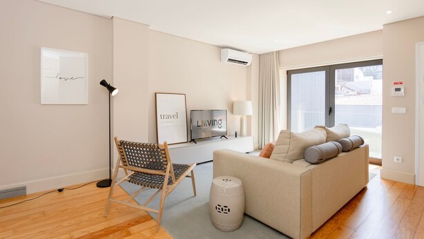 Uma sala de estar moderna com um sofá, uma poltrona, uma televisão e um abajur.