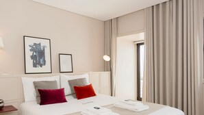Quarto de hotel com uma cama grande, duas almofadas, uma mesa de cabeceira com abajur e um quadro na parede.
