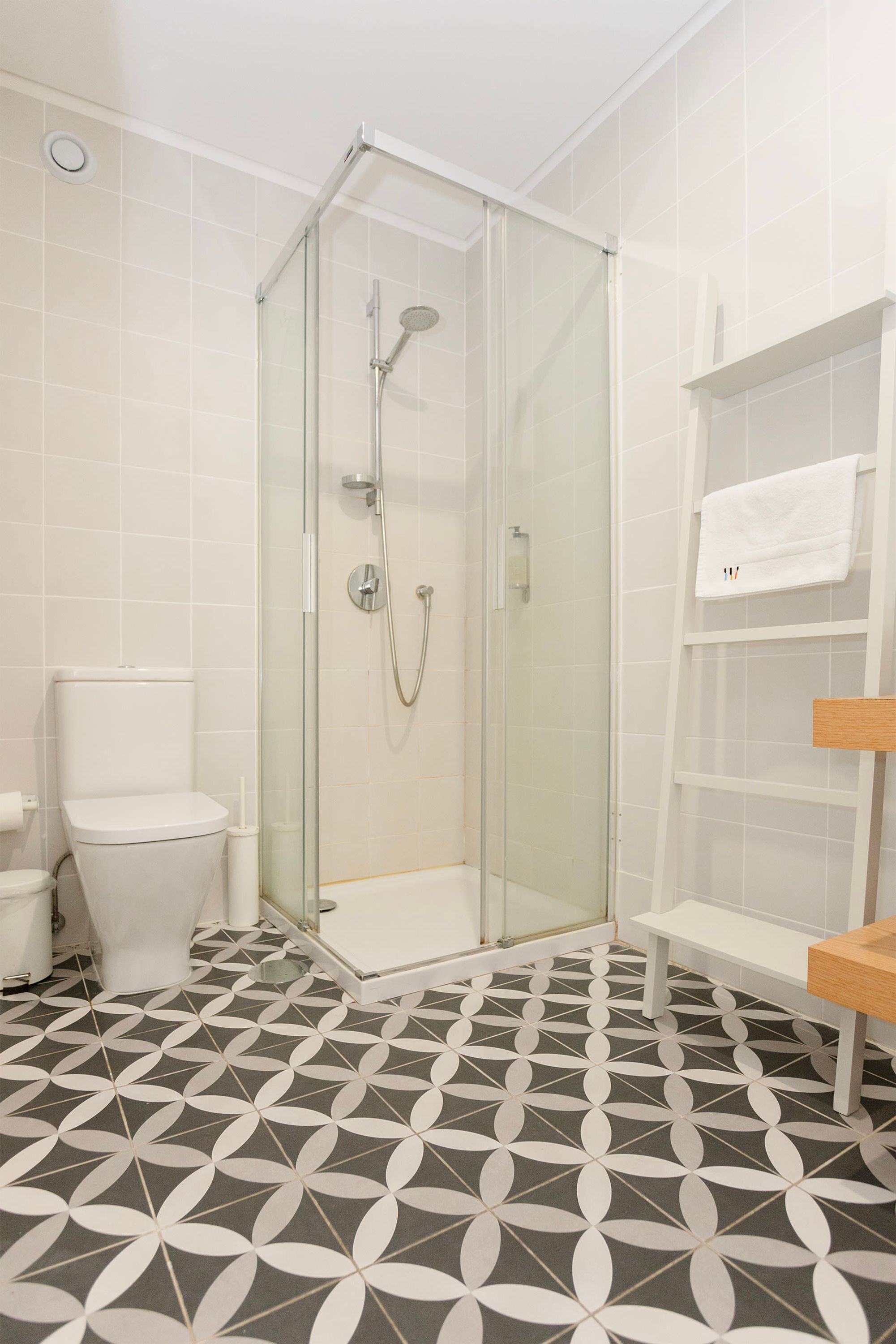 Een badkamer met een douchecabine van glas, witte tegels, een toilet en een plank met een handdoek.