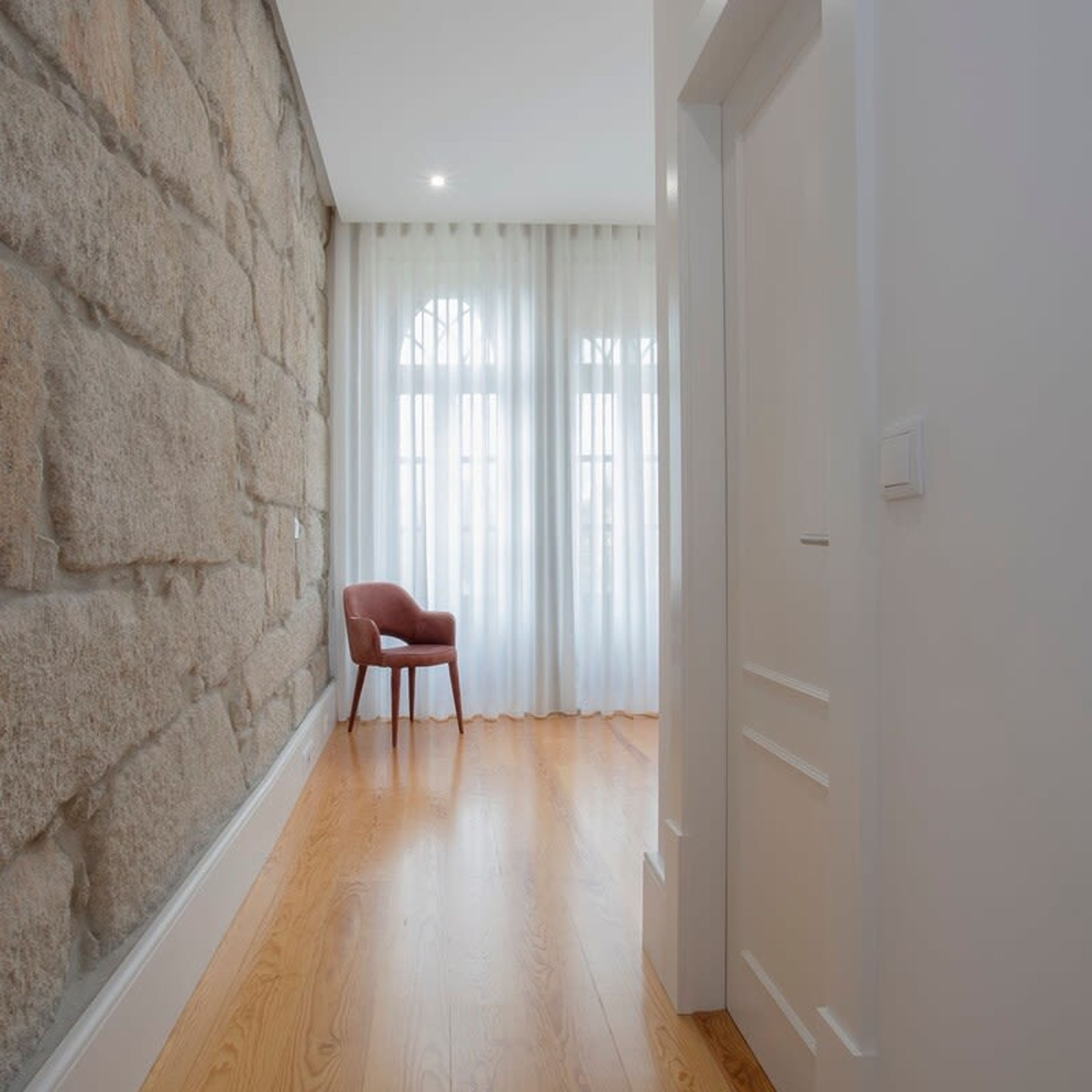 A hallway with a stone wall, a wooden floor, a chair, and a door.