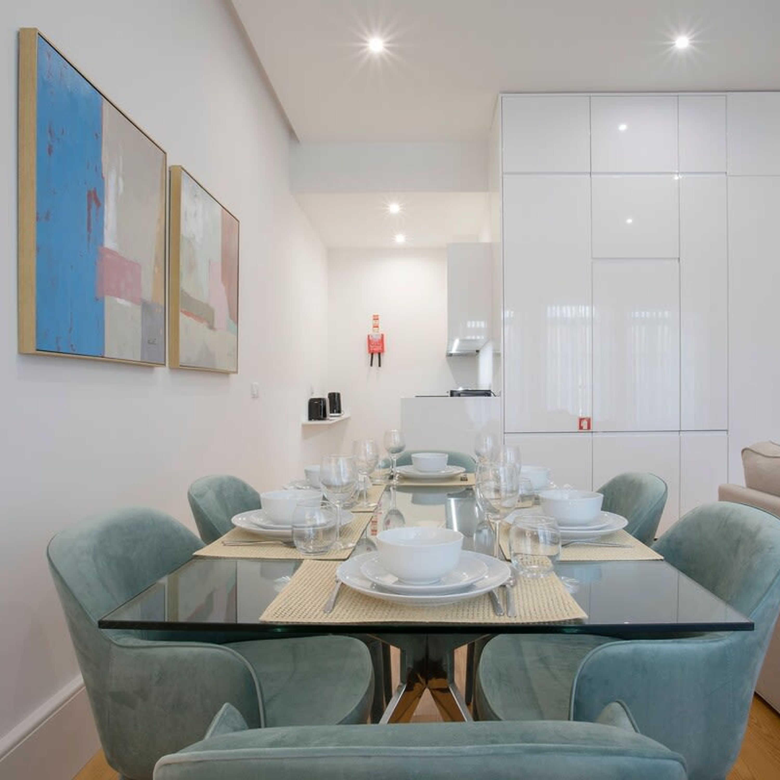 A modern dining area with a glass table, teal chairs, and minimalist decor.