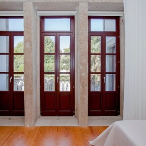 A room with a wooden floor, two dark wooden doors with glass panels, and a view of greenery outside. - Liiiving in Porto Downtown Luxury Apartment 3T (Porto)