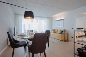 A modern living room with a dining area, featuring a sofa, a coffee table, and a dining table set for four. - Liiiving in Gaia - Beach Seaside Apartment (Vila Nova de Gaia)