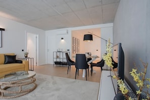 A modern living room with a sofa, a glass coffee table, and a dining area with chairs and a table. - Liiiving in Gaia - Beach Seaside Apartment (Vila Nova de Gaia)