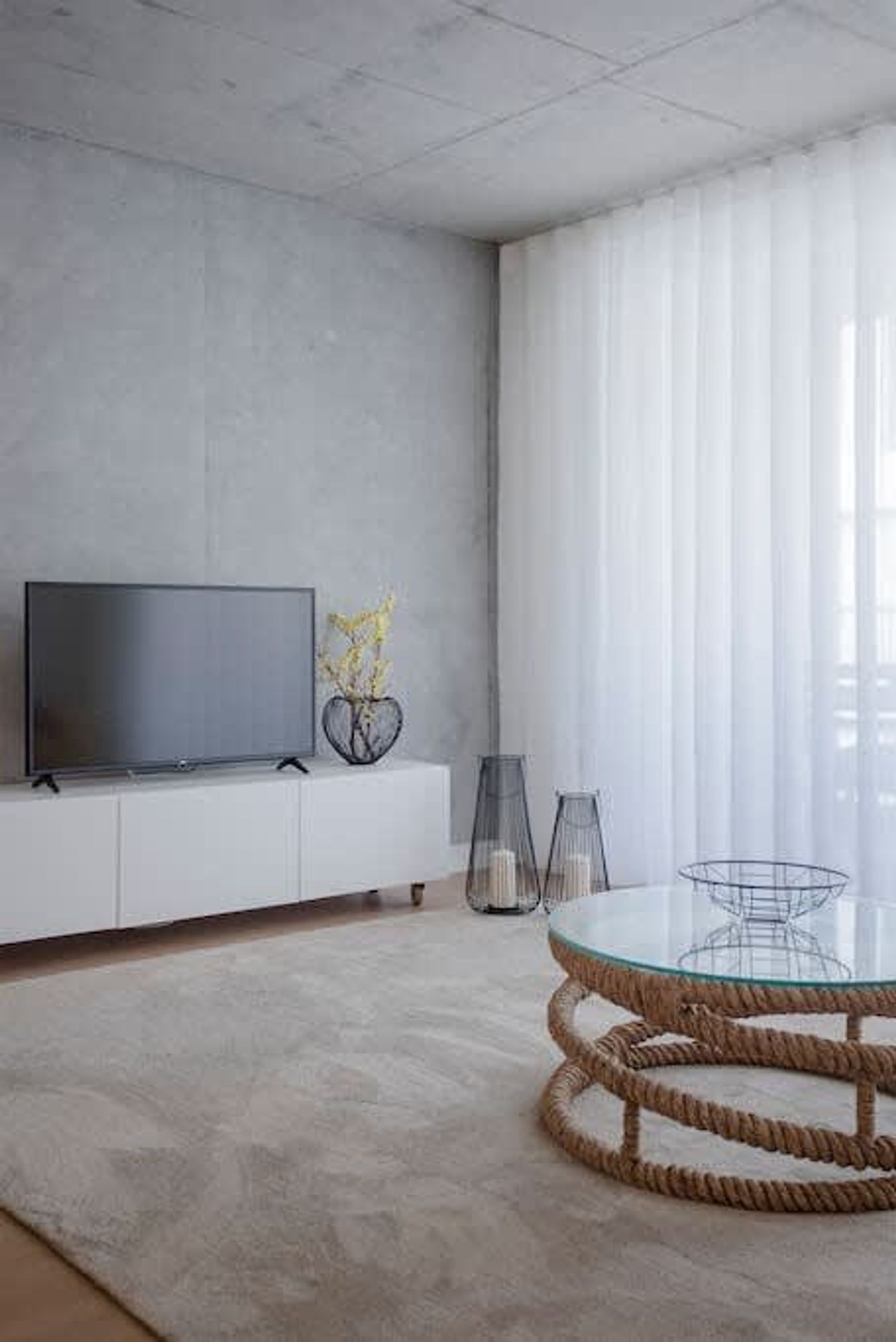 A modern living room with a flat-screen TV, a round glass table, and a white sofa.