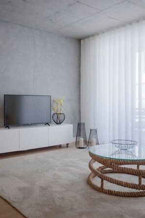 Una sala de estar moderna con un televisor de pantalla plana, una mesa redonda de vidrio y un sofá blanco.