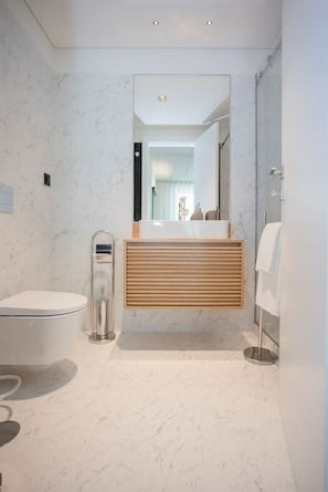 A modern bathroom with a marble floor, a wooden vanity, a glass shower enclosure, and a toilet. - Liiiving in Gaia - Beach Seaside Apartment (Vila Nova de Gaia)