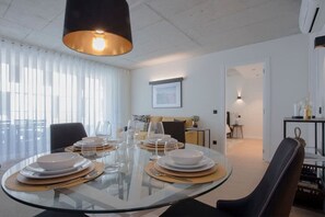 A modern dining area with a round glass table set for four, white plates, and clear glassware. - Liiiving in Gaia - Beach Seaside Apartment (Vila Nova de Gaia)