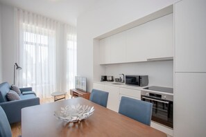 A modern kitchen with white cabinets, a microwave, and an oven. There is a dining table with chairs and a decorative bowl on it. - Liiiving in Porto City View Apartment 1F (Porto)