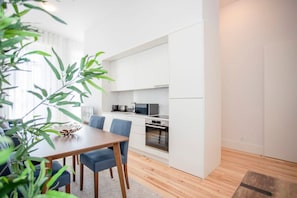 Una cucina moderna con mobili bianchi, un forno a microonde e un fornello. C'è una zona pranzo con un tavolo di legno e sedie blu.
