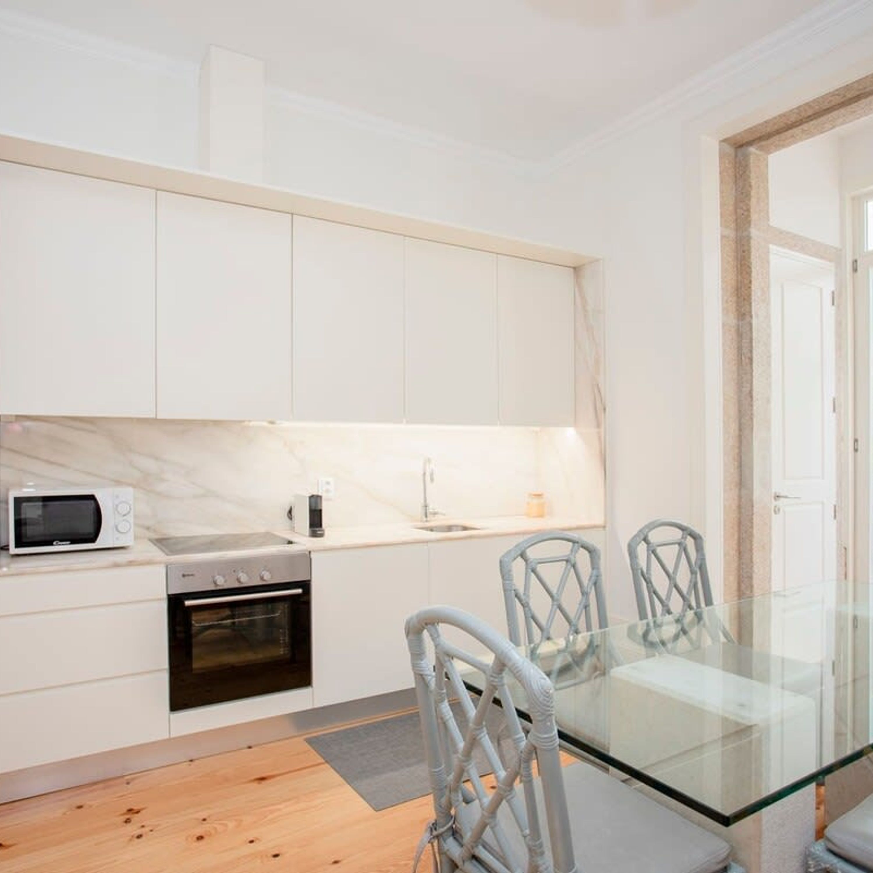 A modern kitchen with white cabinets, a microwave, an oven, and a glass dining table with chairs.