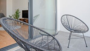 Un salon moderne doté d’une porte coulissante en verre, de deux chaises à structure métallique noire, d’une petite table ronde, d’un téléviseur et d’une plante en pot.