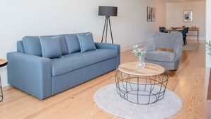 Un salon moderne avec un canapé bleu, un fauteuil gris, une table basse ronde et un lampadaire.