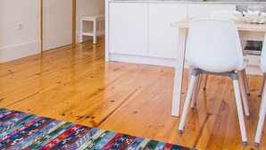 Eine kompakte Küche mit weißen Schränken, einer Marmor-Spritzschutzwand und einem kleinen Essbereich mit weißem Tisch und Stuhl.