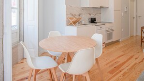 Una cucina moderna con mobili bianchi, una parete rivestita in marmo e un tavolo da pranzo in legno con sedie bianche.