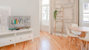 Un soggiorno moderno con una parete decorata in pietra, un tavolo da pranzo in legno con sedie bianche, una TV su un mobile bianco e una pianta su una scala di legno.