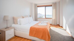 Una camera d'albergo con un letto grande, un comodino, una lampada e una finestra vista mare.