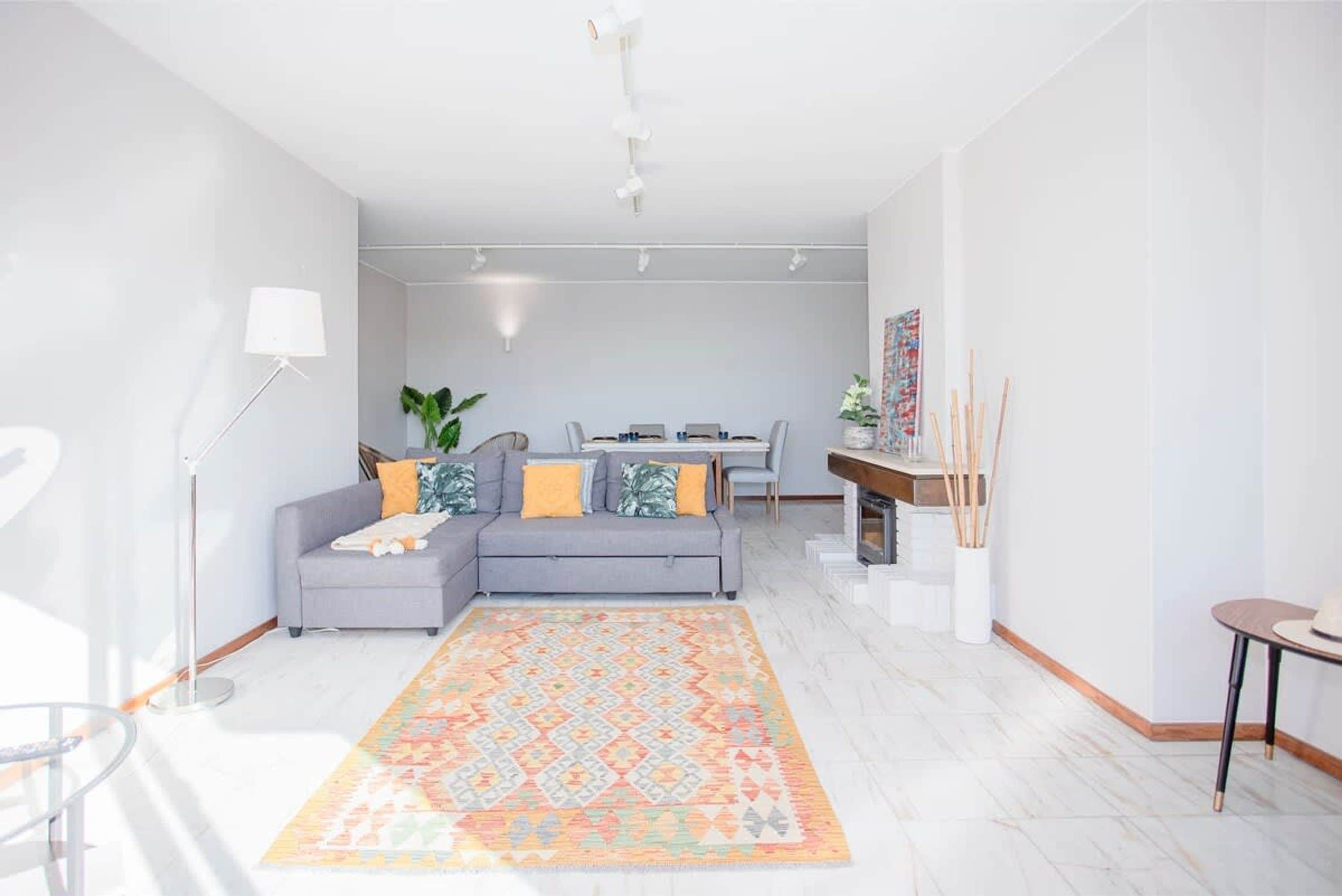 Una sala de estar moderna con un sofá gris, un tapete estampado y un comedor con mesa y sillas.