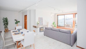 A modern living room with a grey sofa, a dining table with white chairs, and a kitchen area in the background. - Liiiving in Porto Sea River View Apartment (Porto)