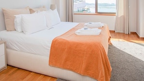 A hotel room with a large bed, a nightstand, a window with curtains, and a view of the sea. - Liiiving in Porto Sea River View Apartment (Porto)