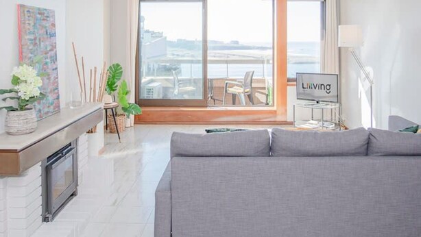 Un soggiorno moderno con un divano grigio, una televisione e una grande finestra con vista su un balcone.