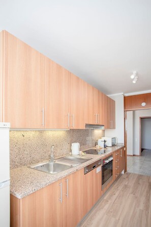 Ett modernt kök med träskåp, bänkskivor i granit, rostfria vitvaror och en inbyggd diskmaskin.