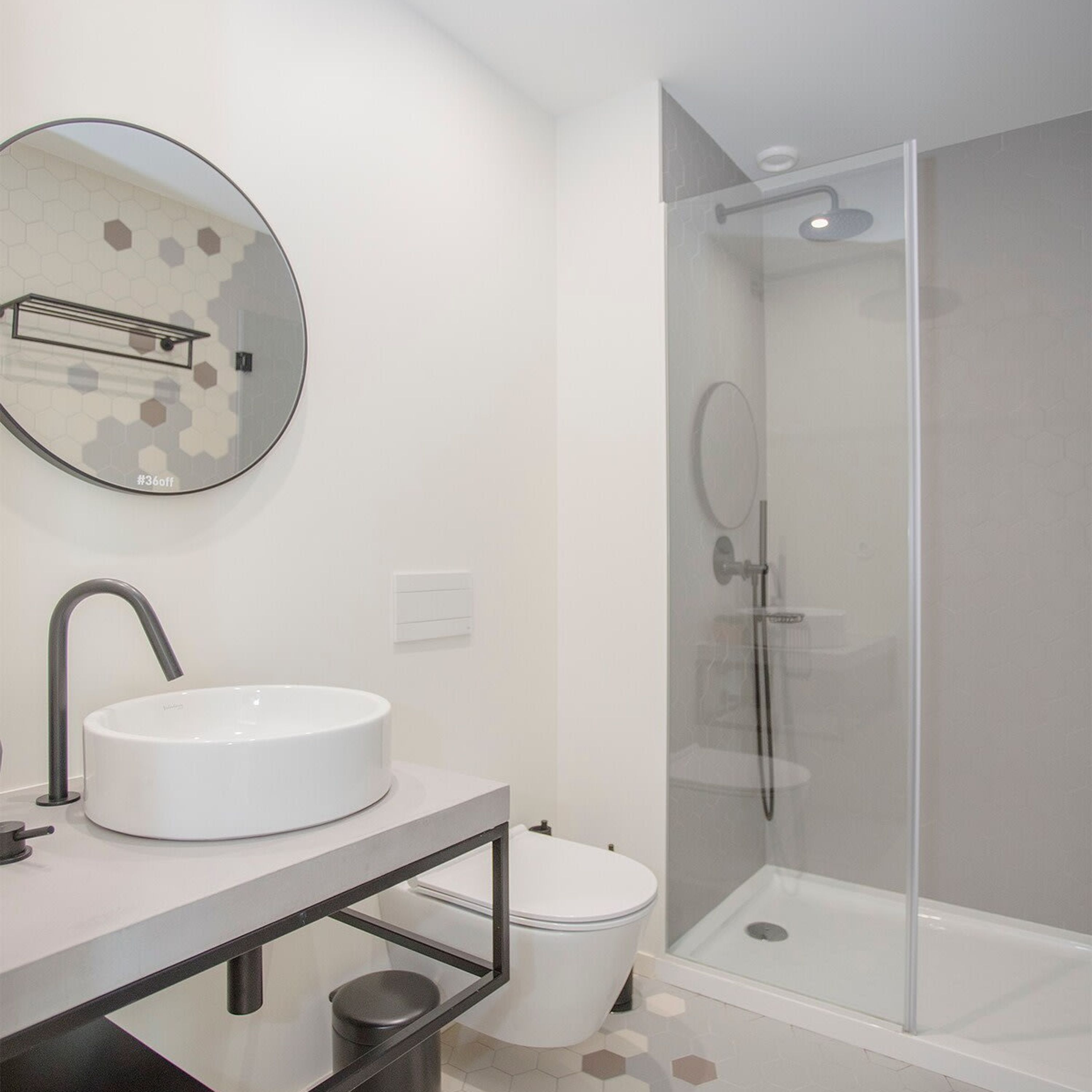 Un baño moderno con un espejo redondo, un lavamanos blanco, un inodoro y una ducha con mampara de vidrio.