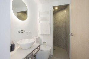 Une salle de bain moderne avec un grand miroir ovale, un lavabo sur colonne blanc, des toilettes et un espace douche.