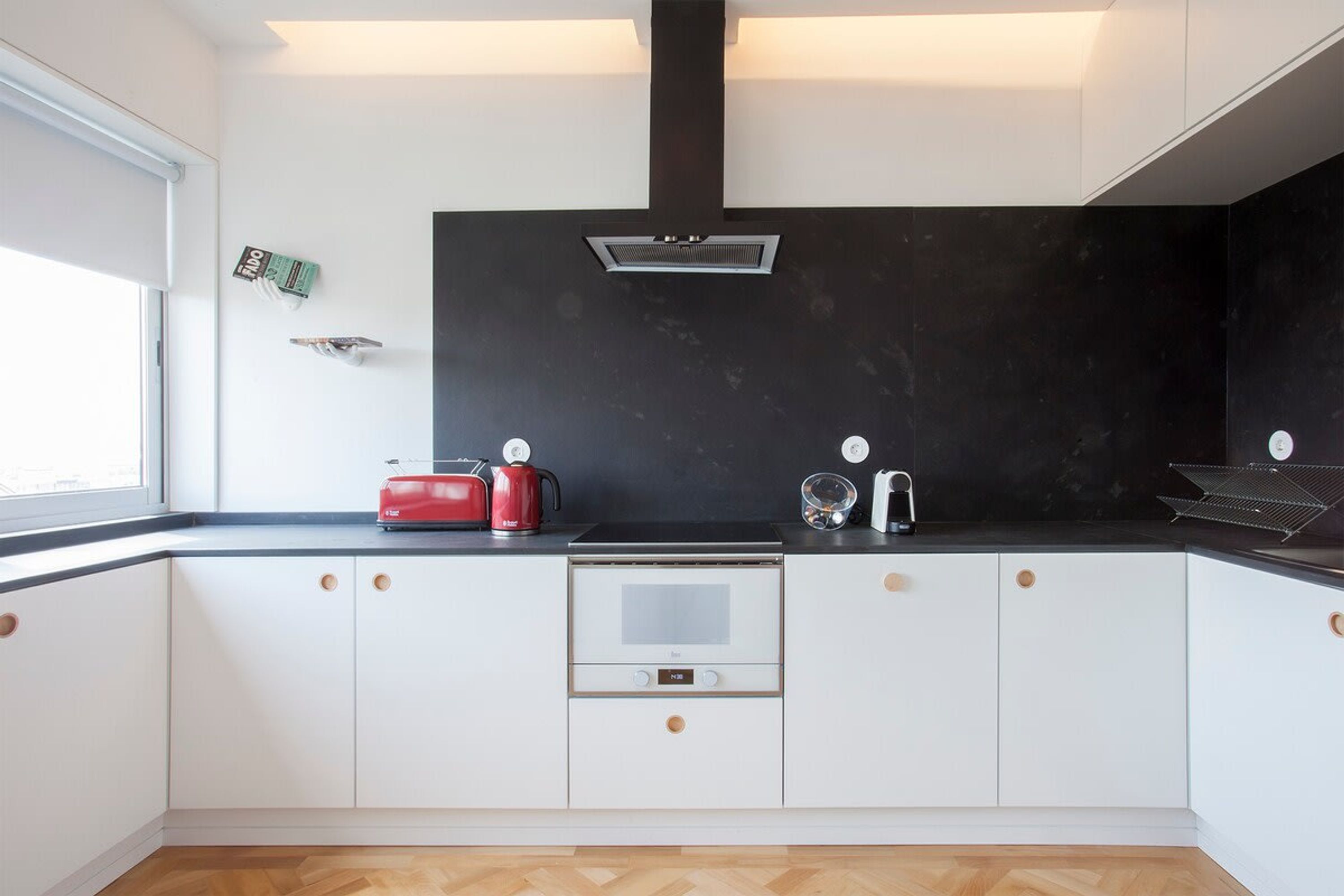 Una cocina moderna con armarios blancos, encimera negra, horno empotrado y campana extractora.