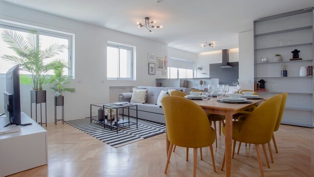 Ein modernes Wohnzimmer mit Essbereich, Küche und großem Fenster mit Pflanzen.