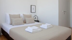 Ein schlicht eingerichtetes Hotelzimmer mit Bett, Nachttisch, gerahmtem Bild und Tür.