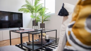 Ein modernes Wohnzimmer mit Flachbildfernseher, einem Glastisch, einer Topfpflanze und einem Streifen Teppich.